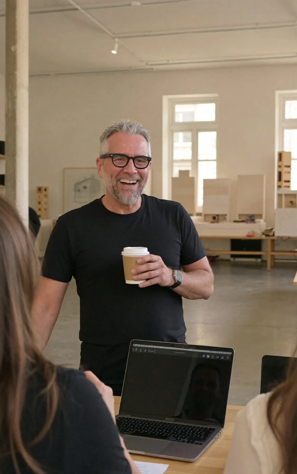 Marc Kleinmann laughing with a coffee in a studio full of architecture models