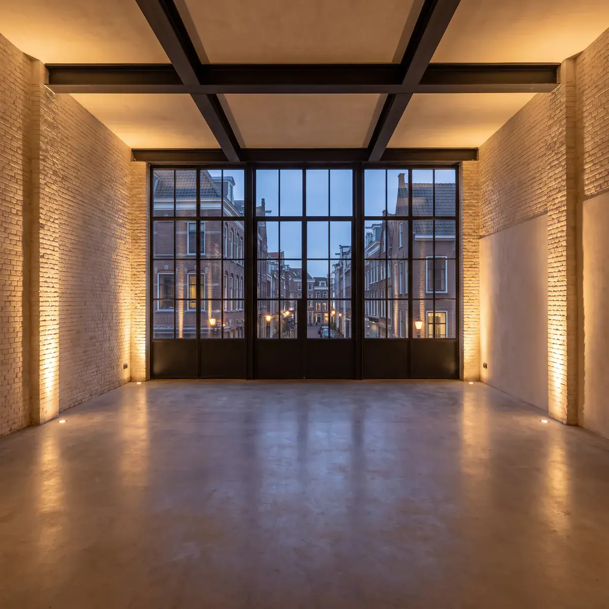 An empty industrial loft event space at evening, with tall windows and a concrete floor